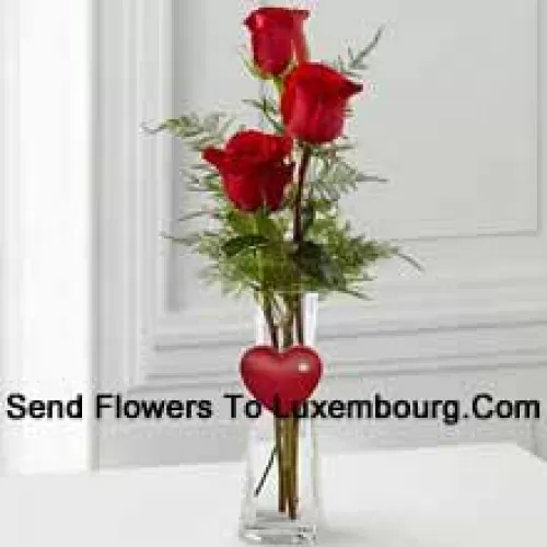 3 Red Roses In A Glass Vase Having A Small Heart Attached To It